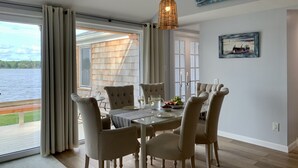 A dining area with a table set for four, a view of the lake, and a painting on the wall. - Cape Code Waterfront Cottage (Dennis Port)
