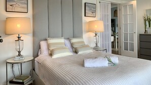 A neatly made bed with a striped duvet, two bedside lamps, and a framed picture on the wall. - Cape Code Waterfront Cottage (Dennis Port)