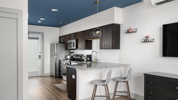 Una cocina moderna con armarios oscuros, electrodomésticos de acero inoxidable y una isla central con taburetes de bar.