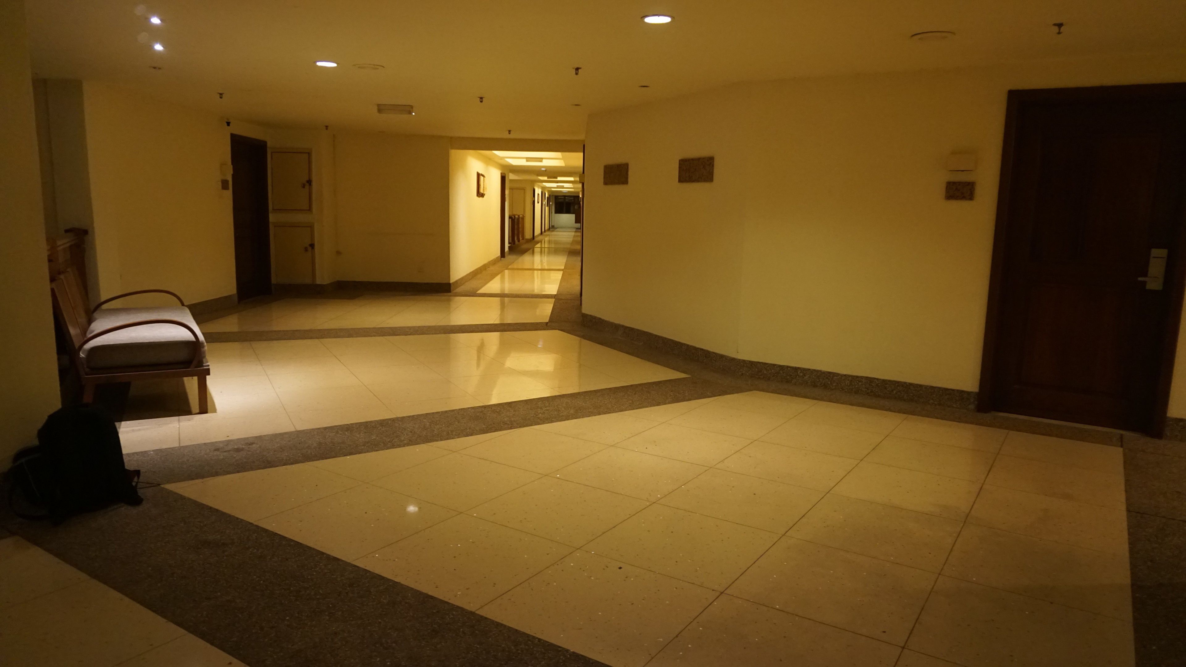 A hotel corridor with a tiled floor, a chair, and a door on the right.