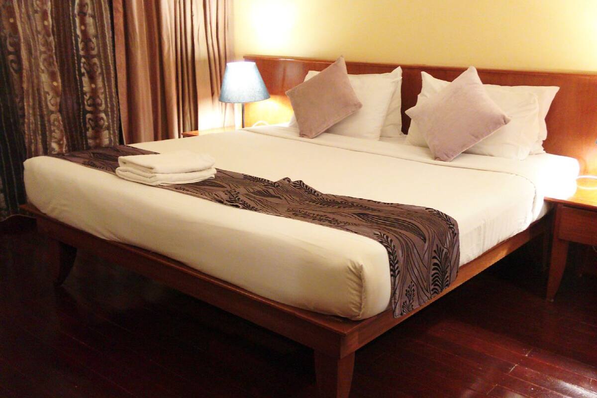 A neatly made bed with a patterned throw, a wooden headboard, and a nightstand with a lamp.