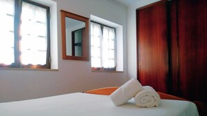 A hotel room with a bed, two windows with curtains, a wooden wardrobe, and a mirror on the wall. - Casa Azul, Carregal, Óbidos (Óbidos)
