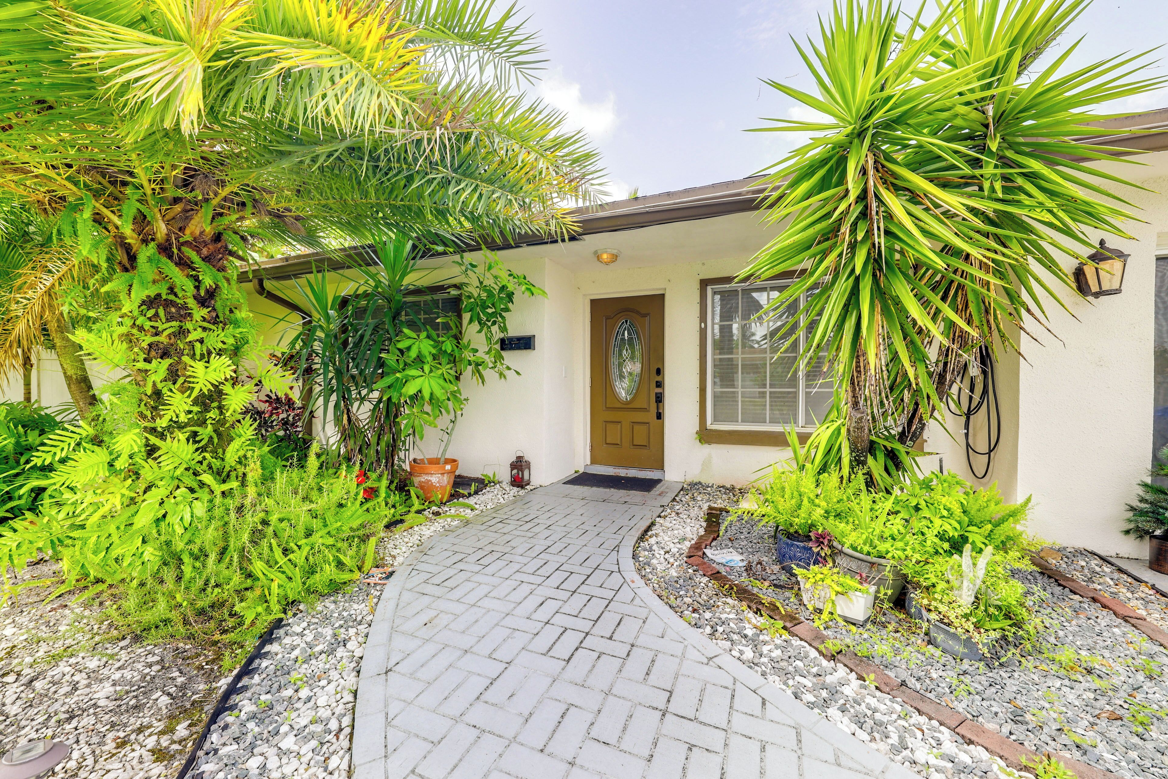 A house with a paved entrance, surrounded by various plants and a small garden area.
