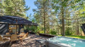 Une terrasse en bois avec un jacuzzi, un espace salon extérieur et une zone couverte comprenant une table et des chaises.