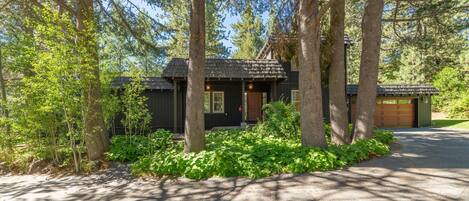 A cabin surrounded by trees with a gravel driveway and a garage.