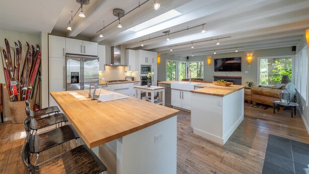 Une cuisine moderne avec un îlot central, des meubles blancs et un plan de travail en bois. Des paires de skis sont appuyés contre le mur, ce qui indique que l’endroit est situé près d’une station de ski.