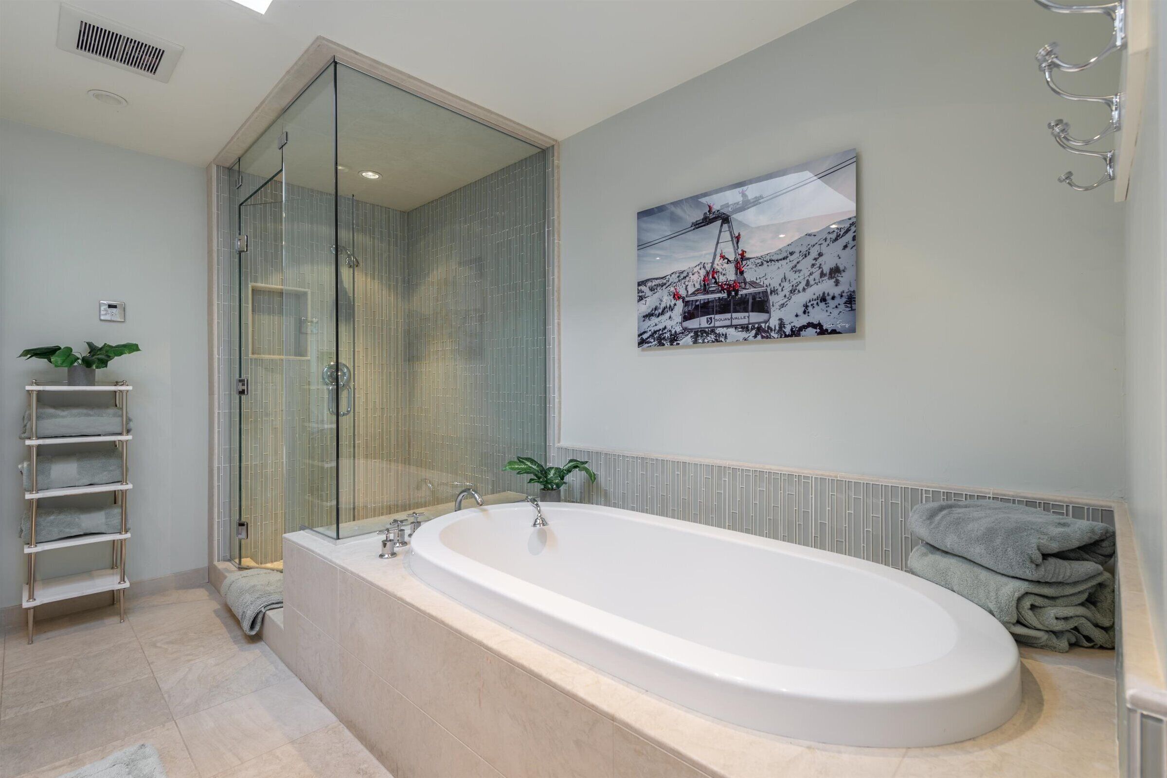 A modern bathroom with a large bathtub, a glass shower enclosure, and a wall-mounted picture of a ski lift.
