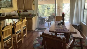 A kitchen with wooden cabinets, a dining area with a table and chairs, and a view of the outdoors through a sliding glass door.