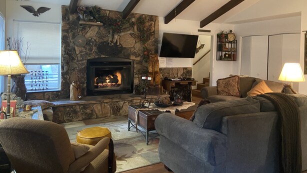 A cozy living room with a stone fireplace, a ceiling fan, and a flat-screen TV mounted on the wall.