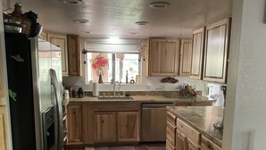 A kitchen with wooden cabinets, a stainless steel refrigerator, a sink, and a window with a vase of flowers.