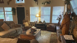 A cozy living room with a sofa, armchair, and a coffee table. There is a lamp on the table and a fireplace with decorative items.