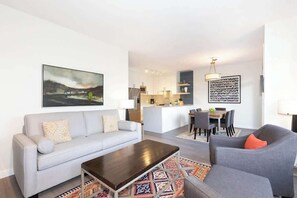 A modern living room with a sofa, a coffee table, and a dining area with chairs and a table.