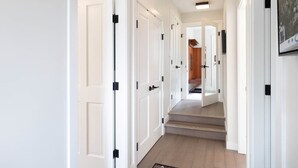 Un pasillo con puertas blancas, una escalera de madera y un cuadro en la pared.
