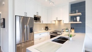Una cocina moderna con electrodomésticos de acero inoxidable, armarios blancos y salpicadero azul.
