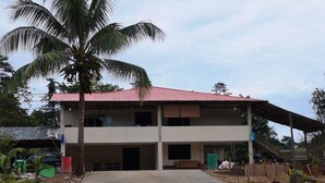 A two-story building with a red roof, a covered porch, and a dirt ground. - Mulu Diana Homestay (Mulu)