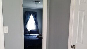 Un corridoio stretto che porta a una camera da letto con un letto, una finestra con tende e una porta.