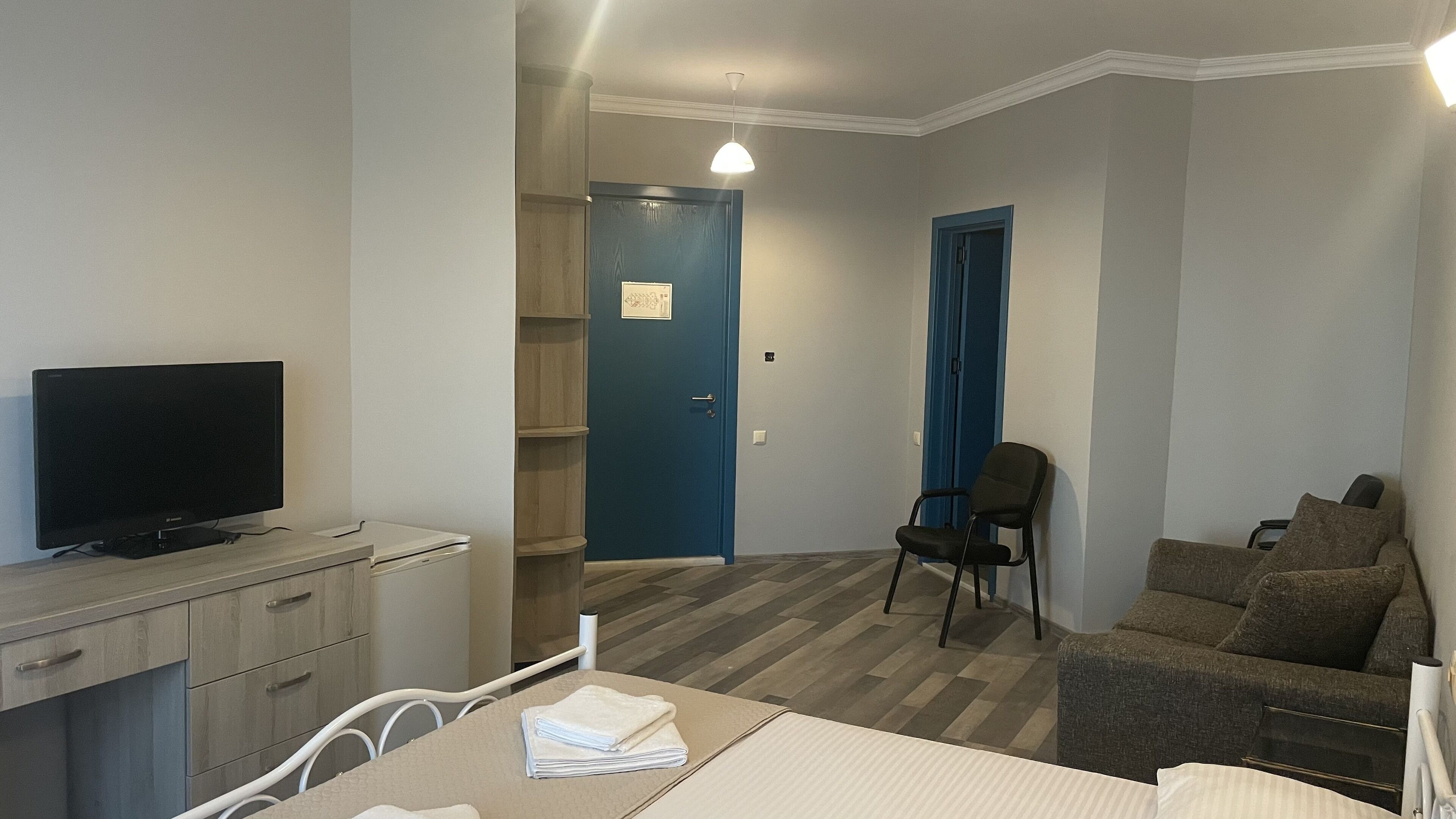 Un espacio habitable compacto con un televisor sobre un mueble de madera, una mesa de comedor con una silla, un sofá y una puerta azul que da a un pasillo.