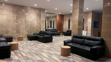 A modern lobby with black leather sofas, wooden coffee tables, and a herringbone-patterned floor.