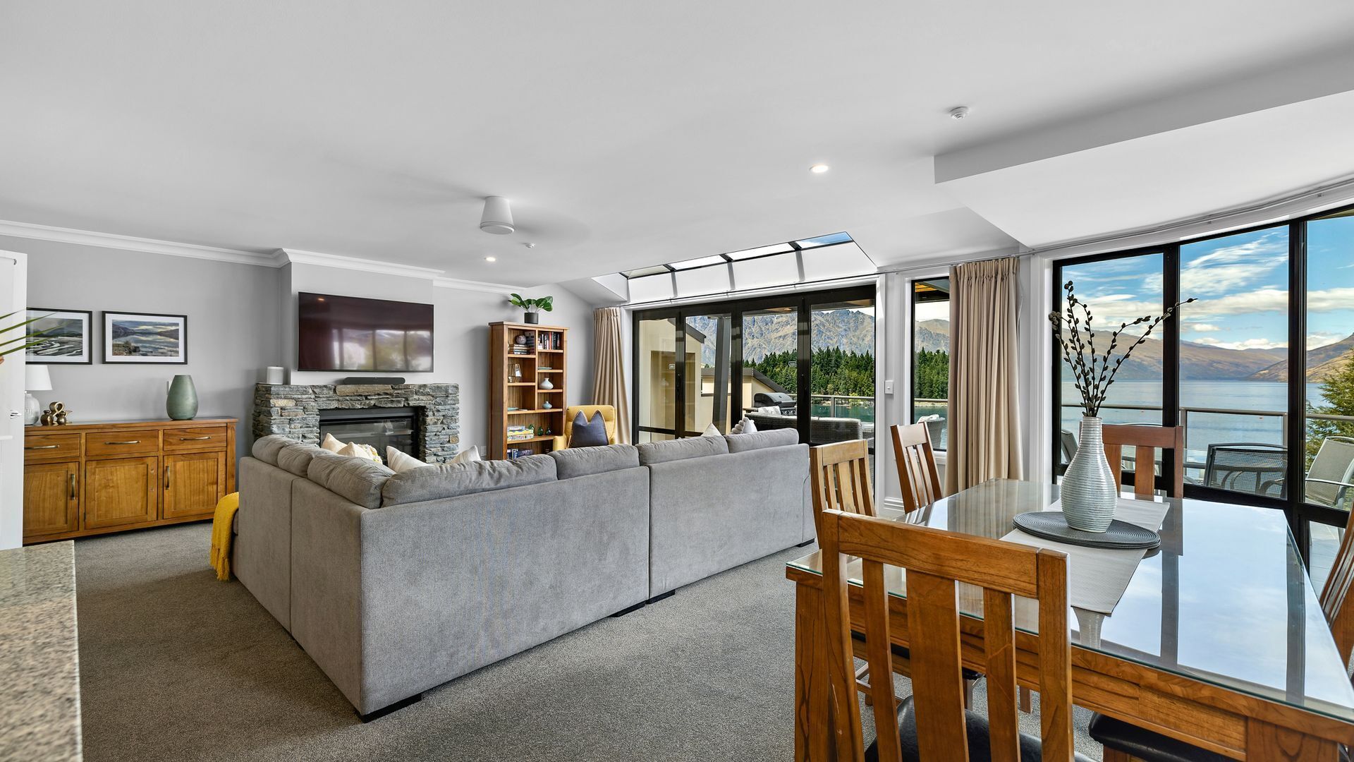 A modern living room with a grey sofa, wooden dining table, and a fireplace.