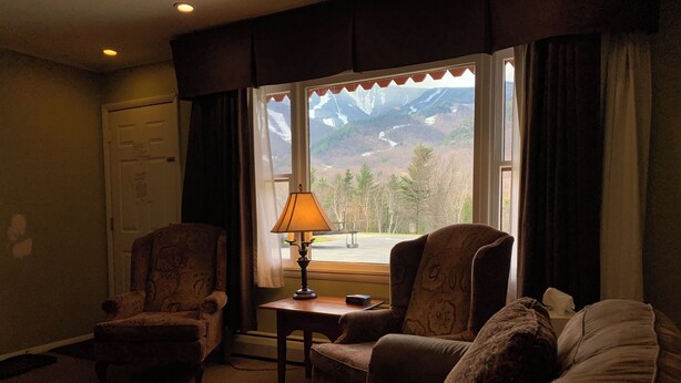 Una sala de estar con dos sillones, un sofá, una lámpara y vistas a montañas a través de una ventana.