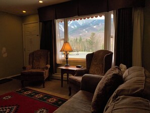 Un salon avec deux fauteuils, un canapé, une lampe et une vue sur les montagnes par une fenêtre.