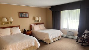 Habitación de hotel con dos camas, una mesita de noche, una silla, un cuadro y una ventana con cortinas.