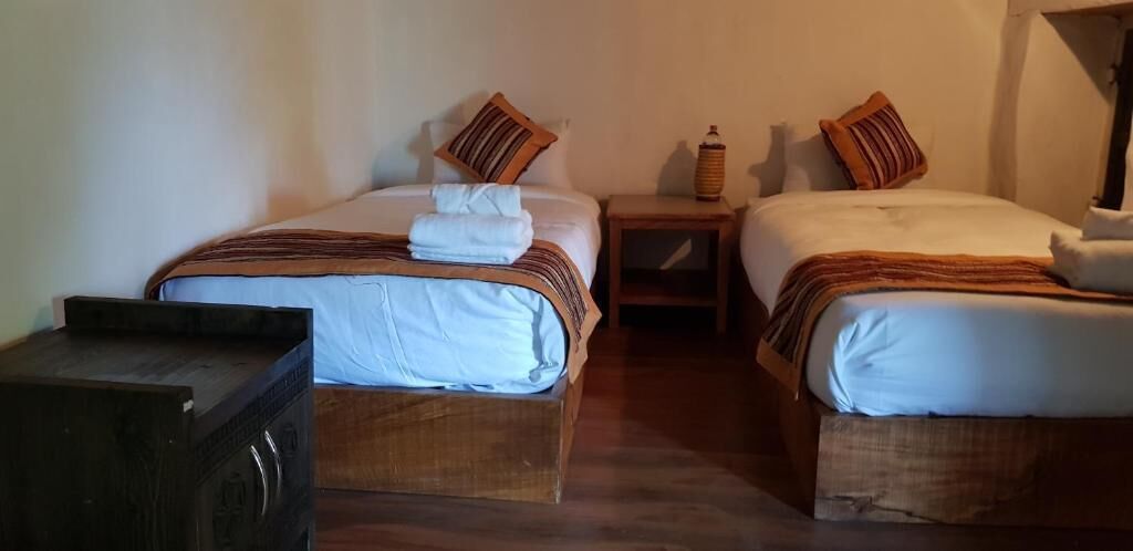 Ein Zimmer mit zwei Betten, jeweils mit einem hölzernen Kopfteil, einem kleinen Nachttisch und einer Lampe.