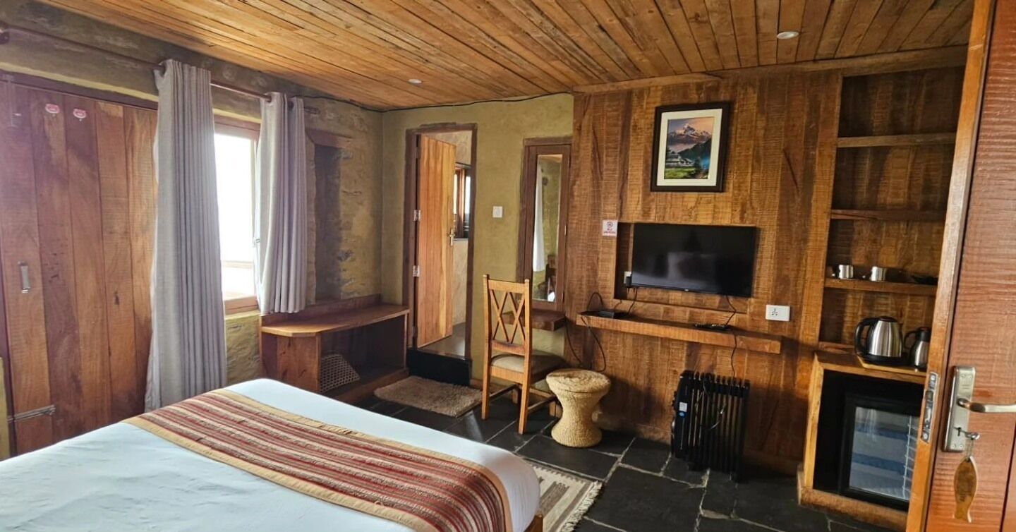 A wooden-paneled room with a bed, a television mounted on the wall, a fireplace, and a stone floor.
