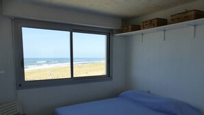 A bedroom with a single bed, a chair, a window with a view of the beach, and storage boxes on the wall. - ATLANTES residence. Flat for 4 persons with ocean view (SOORTS HOSSEGOR)