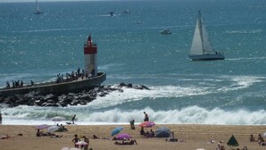 Een strand met een vuurtoren, boten en mensen die van de zee genieten.