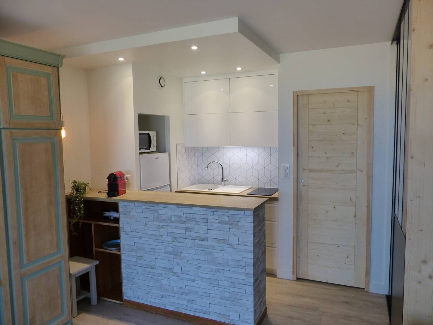 Une cuisine compacte dotée d’un îlot central, de meubles blancs, d’un four à micro-ondes et d’un évier.