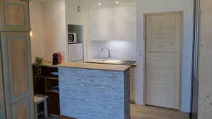 Een compacte keuken met een centraal eiland, witte kasten, een magnetron en een spoelbak.