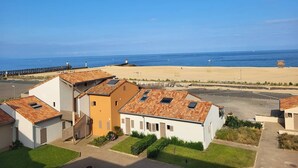 Een woongebied aan de kust, met huizen met pannendaken en een strand op de achtergrond.