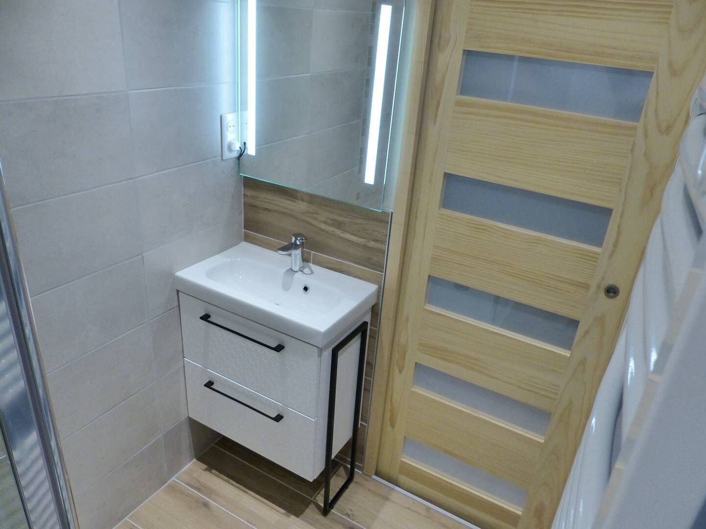 Une petite salle de bain avec un lavabo blanc, un meuble-lavabo en bois et un miroir.