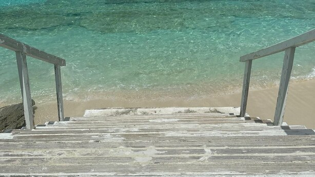 A wooden staircase leading to a beach with clear turquoise water and a clear sky.