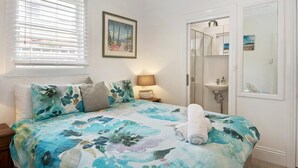 Un dormitorio con cama, una mesita de noche, una lámpara, un cuadro y la puerta del baño.
