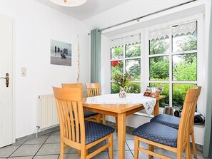 A dining area with a table and chairs, a radiator, a window with lace curtains, and a framed picture on the wall.