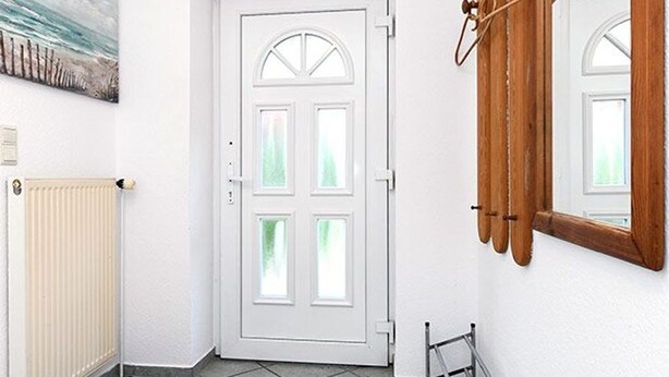 Una puerta blanca con un panel de vidrio, un radiador, un perchero de madera y un espejo en la pared.