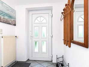Una puerta blanca con un panel de vidrio, un radiador, un perchero de madera y un espejo en la pared.