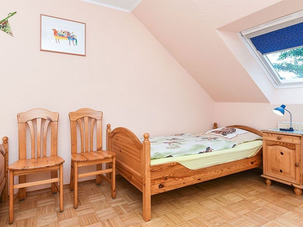 Une chambre à coucher avec un lit en bois, deux chaises, une table de chevet, une fenêtre donnant sur un beau paysage et un tableau encadré accroché au mur.