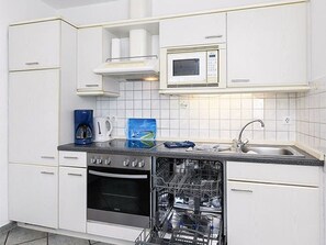 A compact kitchen with white cabinets, a microwave, a coffee maker, and a dishwasher.