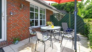 Un patio con una mesa y sillas, un paraguas rojo y un edificio de ladrillo con un ventanal.