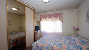 Una camera da letto con due letti, una scrivania con computer, uno specchio, una finestra con tende e una lampada.