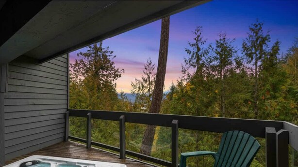 Terraza de madera con jacuzzi y una silla Adirondack verde, con vistas a una zona boscosa.