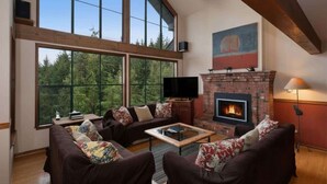 Una sala de estar con chimenea, ventanas grandes y televisor.