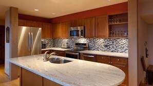 Una cocina moderna con armarios de madera, electrodomésticos de acero inoxidable, encimera de mármol y salpicadero azulejado.