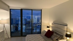 A modern bedroom with a large bed, two bedside tables with lamps, a dresser, and a sliding glass door leading to an outdoor balcony. - Gorgeous modern apartment in the heart of Miami (Miami)