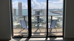 A balcony with two chairs and a small table, overlooking a cityscape with buildings and a body of water. - Gorgeous modern apartment in the heart of Miami (Miami)