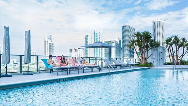 A rooftop pool with lounge chairs and umbrellas, surrounded by palm trees and high-rise buildings in the background. - Gorgeous modern apartment in the heart of Miami (Miami)
