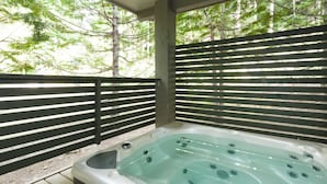 Un jacuzzi con cubierta de vidrio, rodeado por una valla de madera y árboles al fondo.